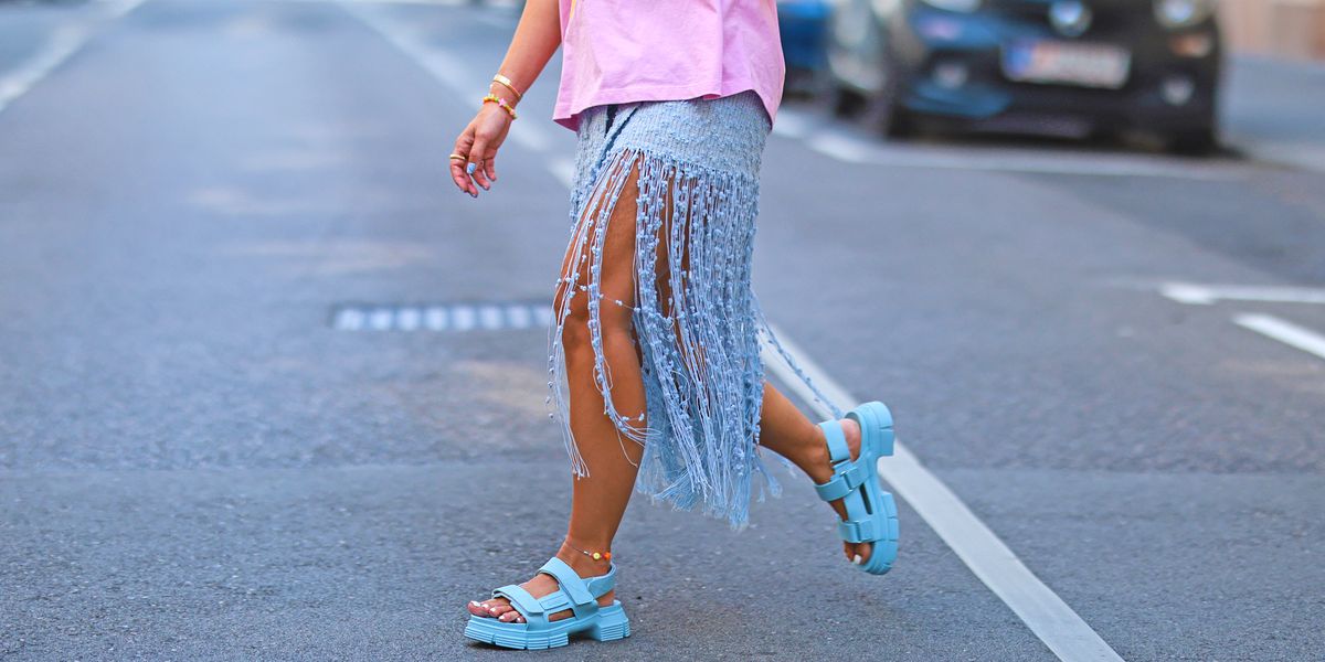 close up shot of woman crossing the street and wearing a long fringed skirt and sandals