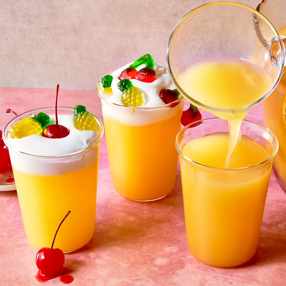 orange punch with round ice balls, sliced oranges, gummy candy, and maraschino cherries in a punch bowl with whipped cream on the side