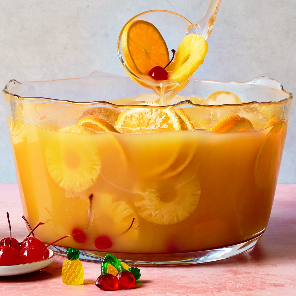 orange punch with round ice balls, sliced oranges, gummy candy, and maraschino cherries in a punch bowl with whipped cream on the side