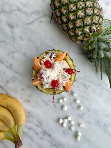fruit salad served in a pineapple bowl with bananas and marshmallows nearby