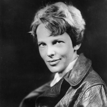 amelia earhart looks at the camera with a small smile on her face, she wears a leather jacket and has short hair