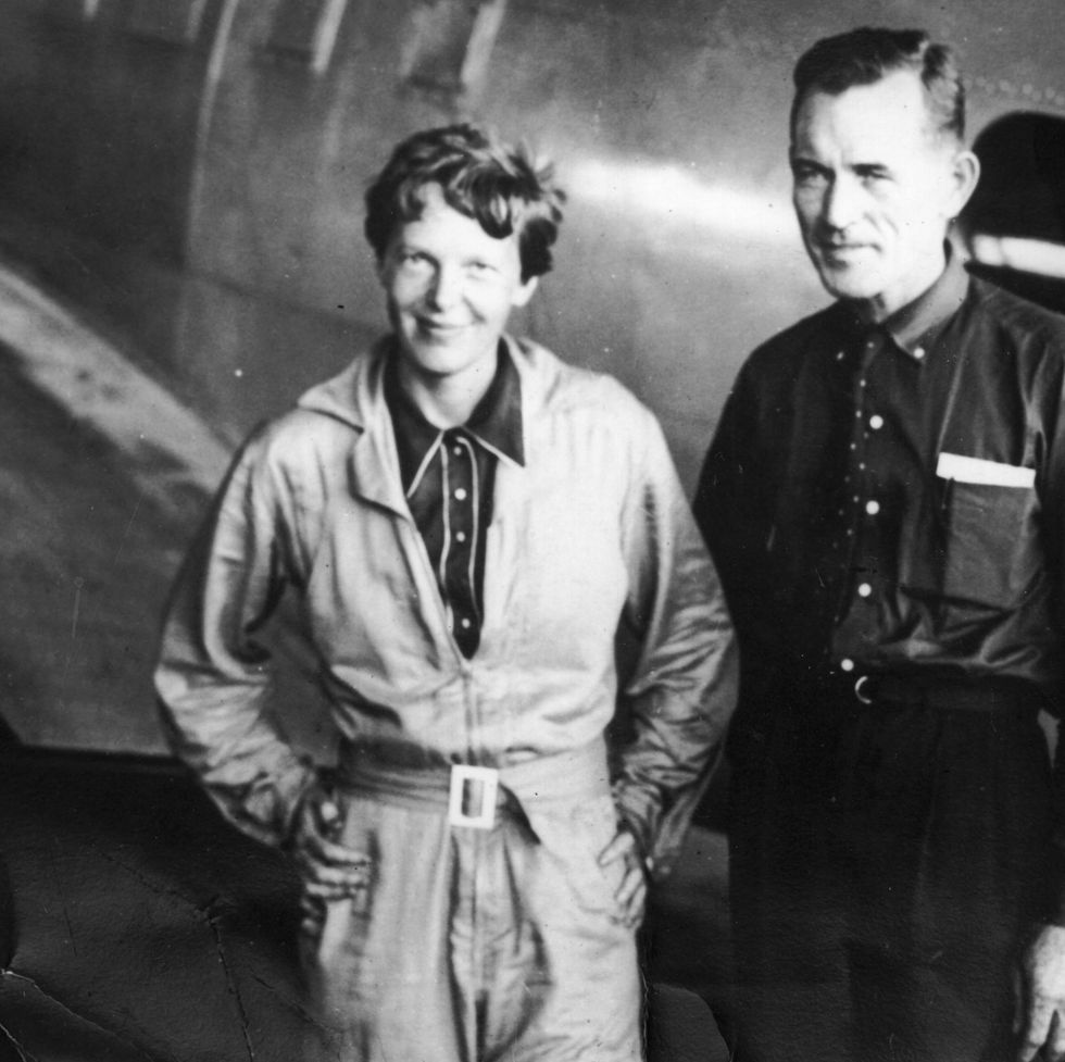 amelia earhart and fred noonan pose for a photo while standing in front of a silver plane