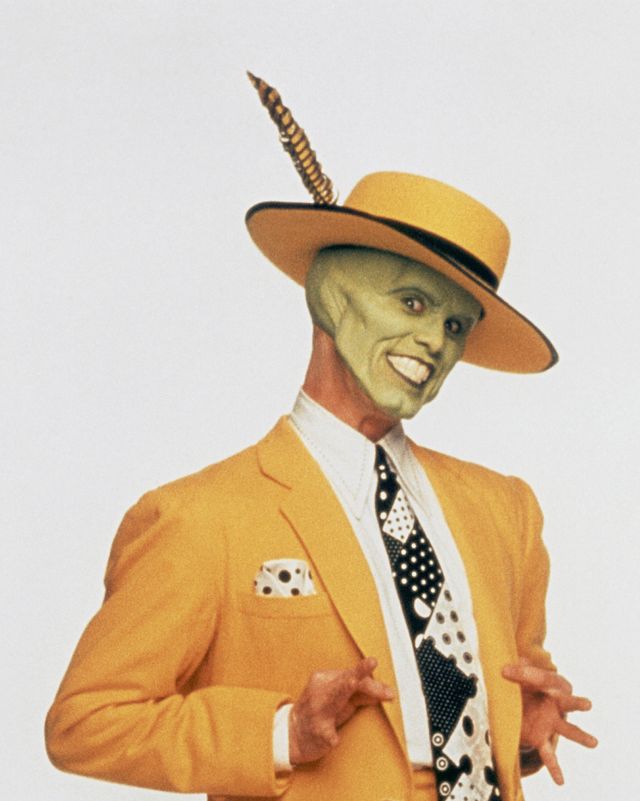 a man smiles while posing in a bright yellow suit and matching hat, his head is covered with green face paint