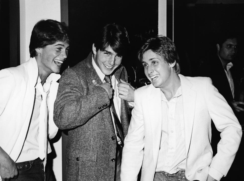 rob lowe, tom cruise, and emilio estevez stand together and smile, they all were suit jackets and dress shirts, lowe and cruise also have on ties