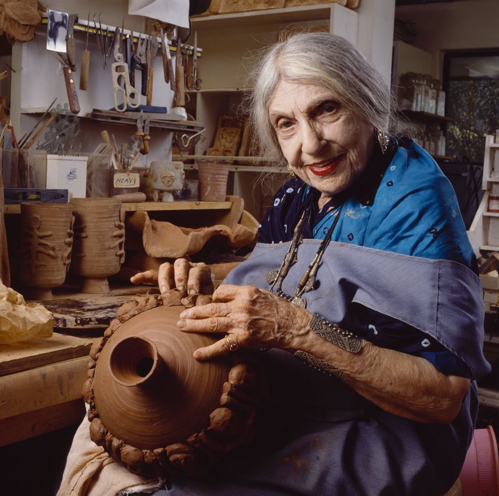beatrice wood, holding a pot and sitting at a desk in her artist's studio