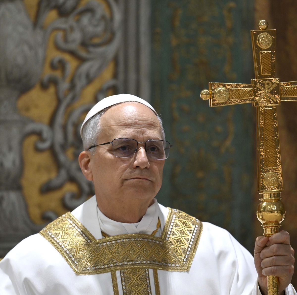 priest in white and gold robes holding a large gold cross