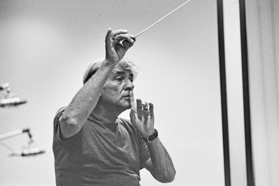a black and white phot of leonard bernstein wearing a t shirt while conducting and using his left hang to make a shush motion