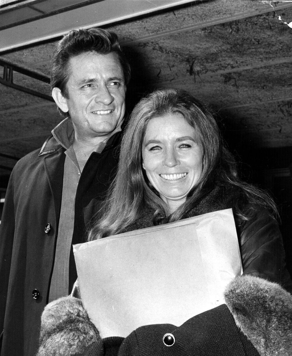 johnny cash smiling as he stands behind wife june carter holding an envelope
