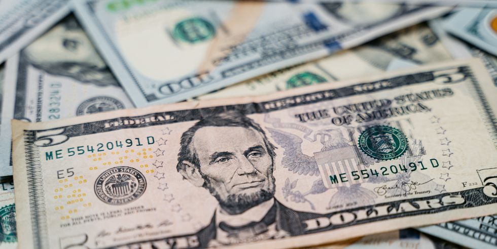 stack of paper bills with a five dollar bill on top featuring a portrait of abraham lincoln facing right