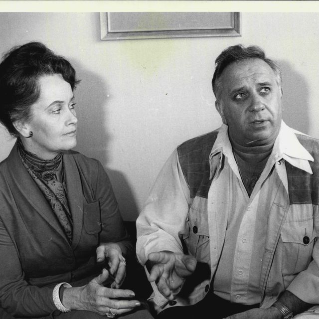 a woman and a man sitting in chairs and gesturing with their hands, she looks at the man and he looks up to the right
