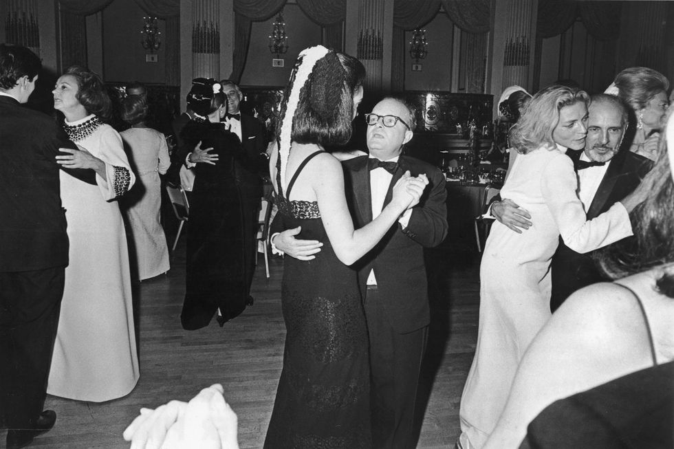 truman capote dances with a woman as they are surrounded by other couples dancing, everyone wears formal attire in the ballroom