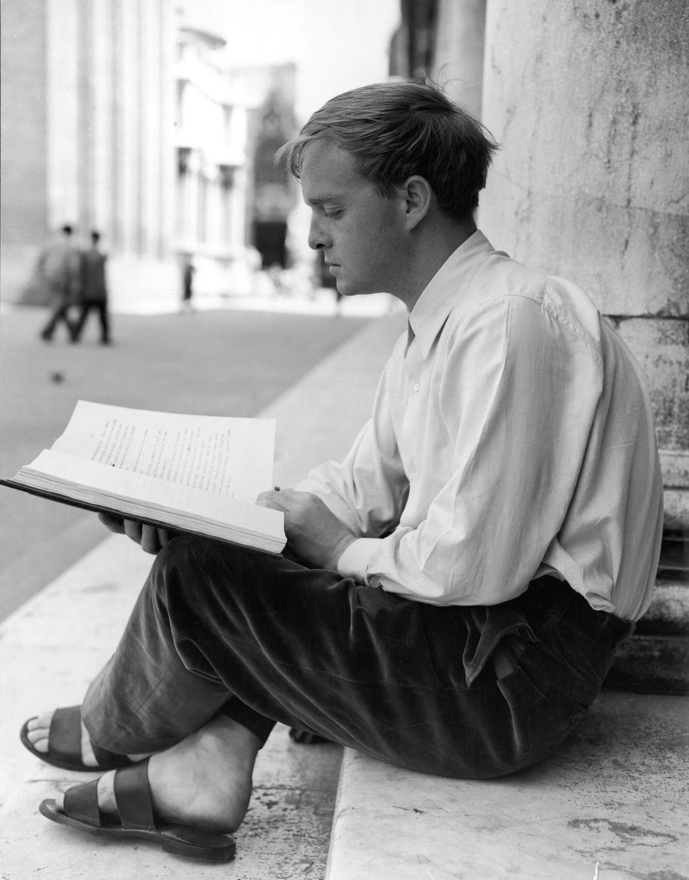 truman capote sits on the steps outside a building and reads a book