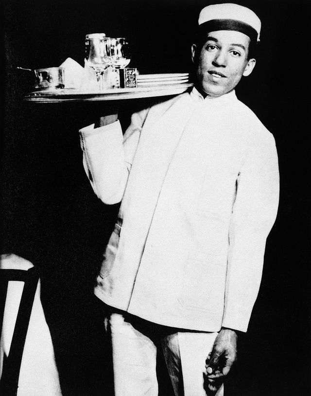 langston hughes holding a tray in the air with his right arm while working as a waiter in a unifrom