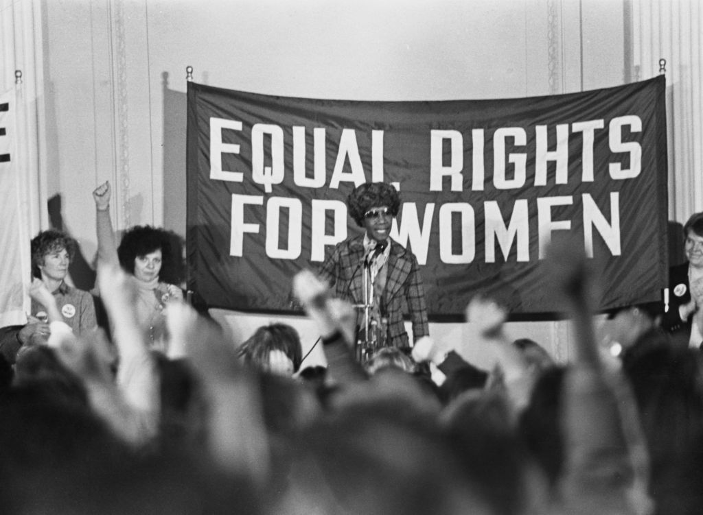 shirley chisholm standing in front of a sign that reads equal rights for women