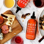 bees knees salted honey on marble kitchen counter surrounded by charcuterie board of sausage cheese nuts peaches crackers and wine