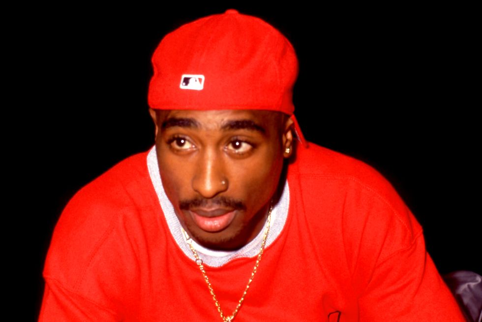 tupac shakur, wearing a red shirt, gold chain, and backwards red hat