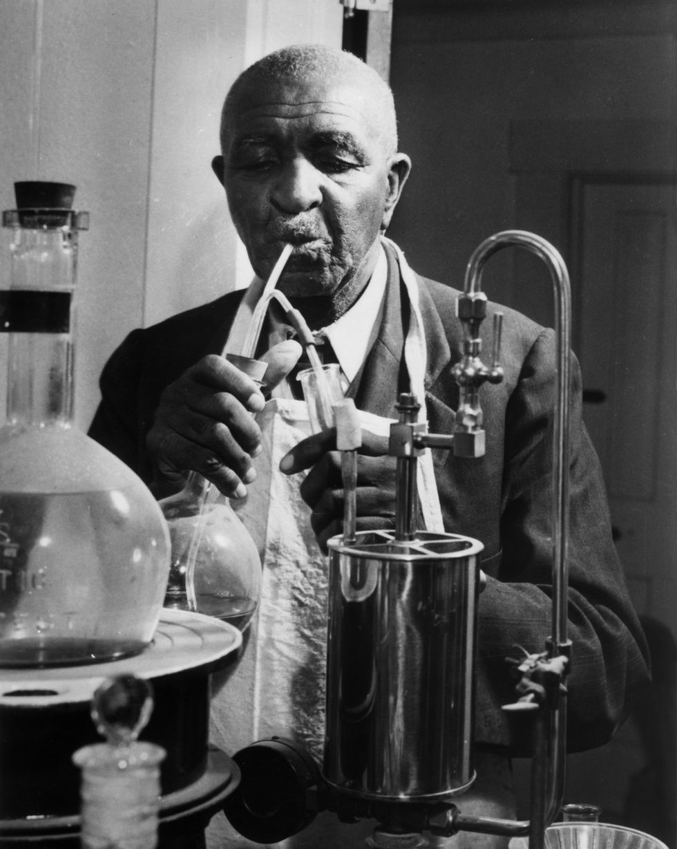 george washington carver holding a beaker and test tube while working on an experiment