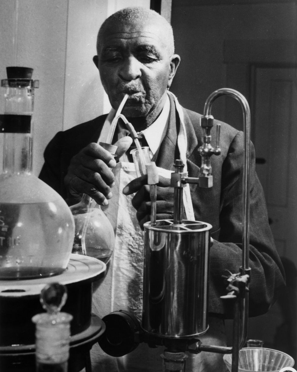 George Washington Carver sosteniendo un vaso de precipitados y un tubo de ensayo mientras trabajaba en un experimento.