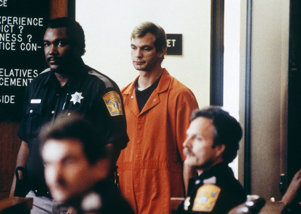 jeffrey dahmer, wearing a orange prison jumpsuit, is escorted by a police officer into a courtroom