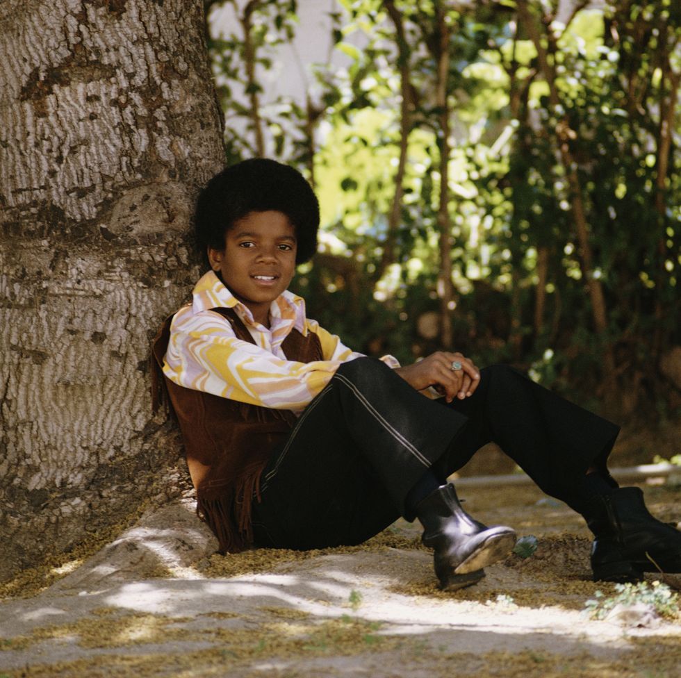 michael jackson sits under a tree as a child, wearing a very 1970s printed outfit