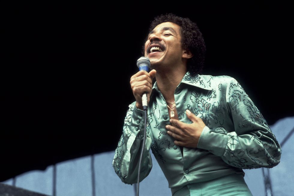 smokey robinson wears a monochrome mint green outfit and sings into a microphone he holds in one hand