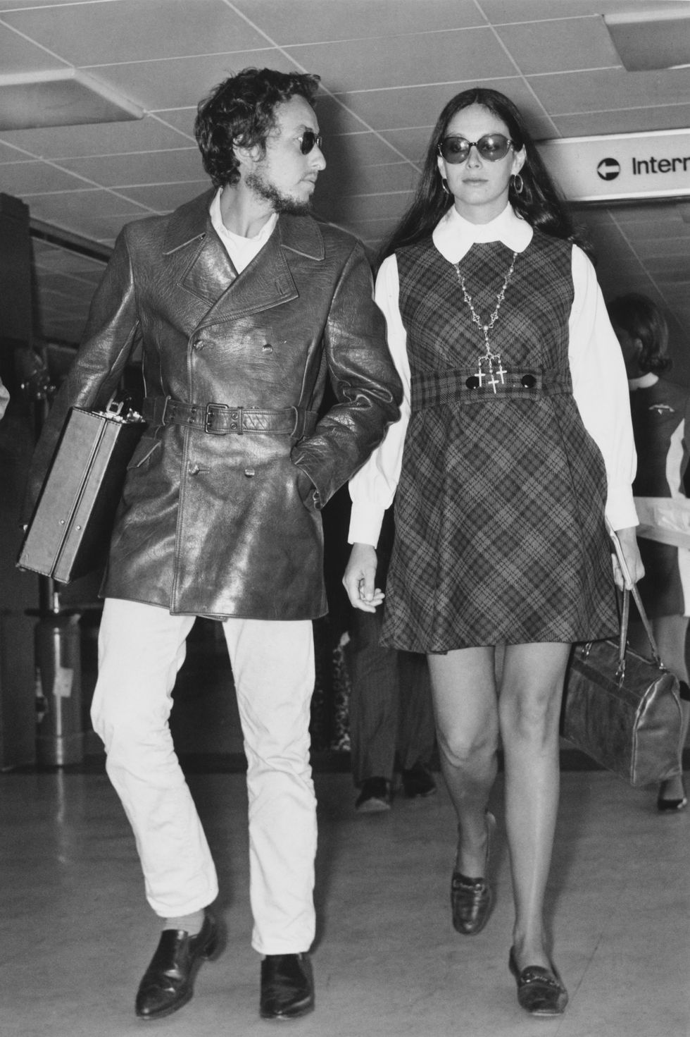 bob dylan and sara lownds walk inside a building, both carry a bag, he looks at her