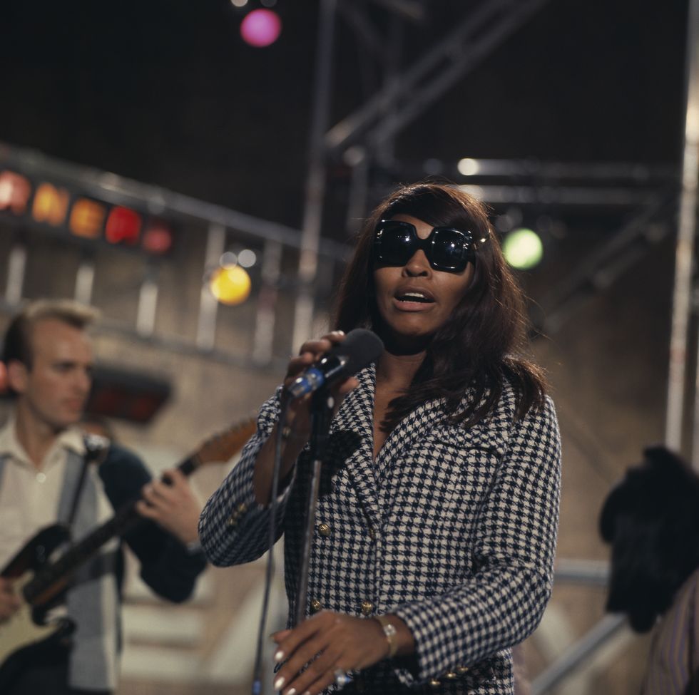 tina turner holds a microphone on a stand and looks at the camera mid performance