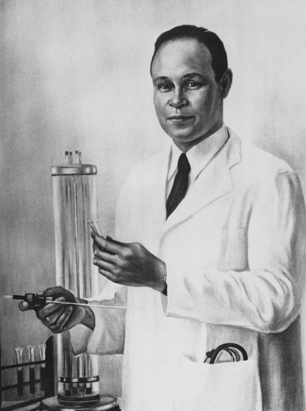charles drew looks directly forward, wearing a lab coat and standing next to laboratory equipment