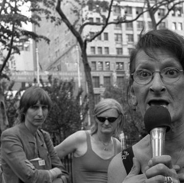 a woman with glasses speaks into a microphone while standing inside an urban park