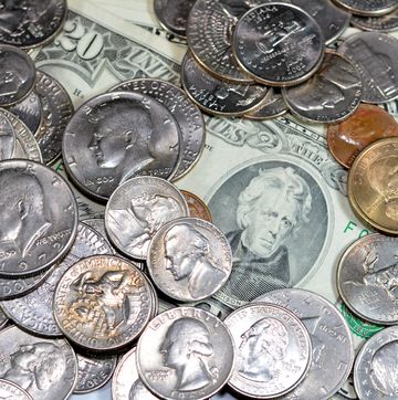 a pile of silver and gold coins over paper banknotes