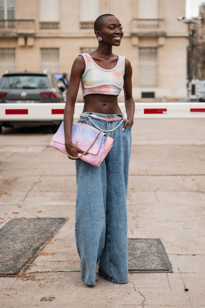 a woman wearing a colorful chanel crop top and bag with baggy jeans and a pearl belt in a roundup of the best travel outfits for women 2024