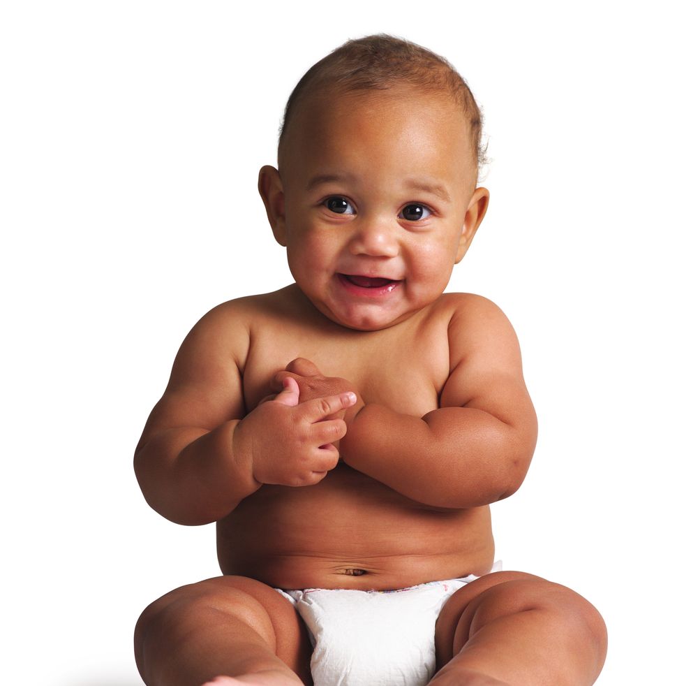 an african american baby sits in a diaper and smiles slightly