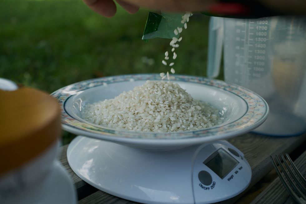 an amount of rice is being weighed over a white plate by using a digital scales some rice is putted onto a plate for weight measurements over a digital scale