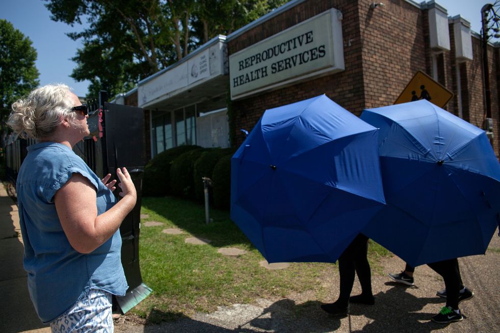 a patient being hidden behind large umbrellas while walking into an abortion clinic