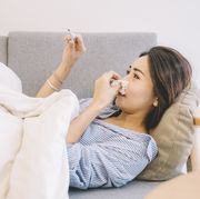 an asian chinese female lying on sofa looking at the thermometer with her pajamas and blanket