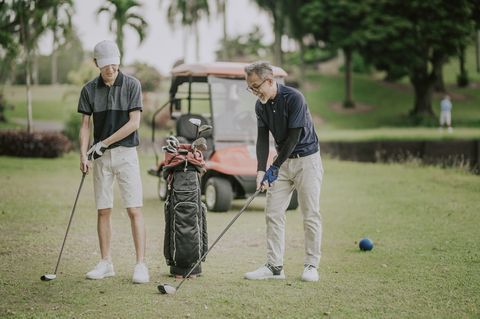 an asian chinese mature adult selecting driver golf club from golf bag for tee off and guiding teaching his son at the golf course tee off point