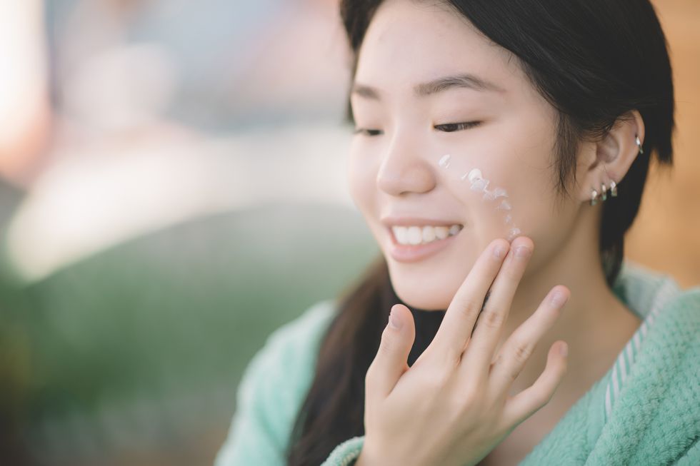 an asian chinese teenager girl applying moisturiser facial cream on hand and face