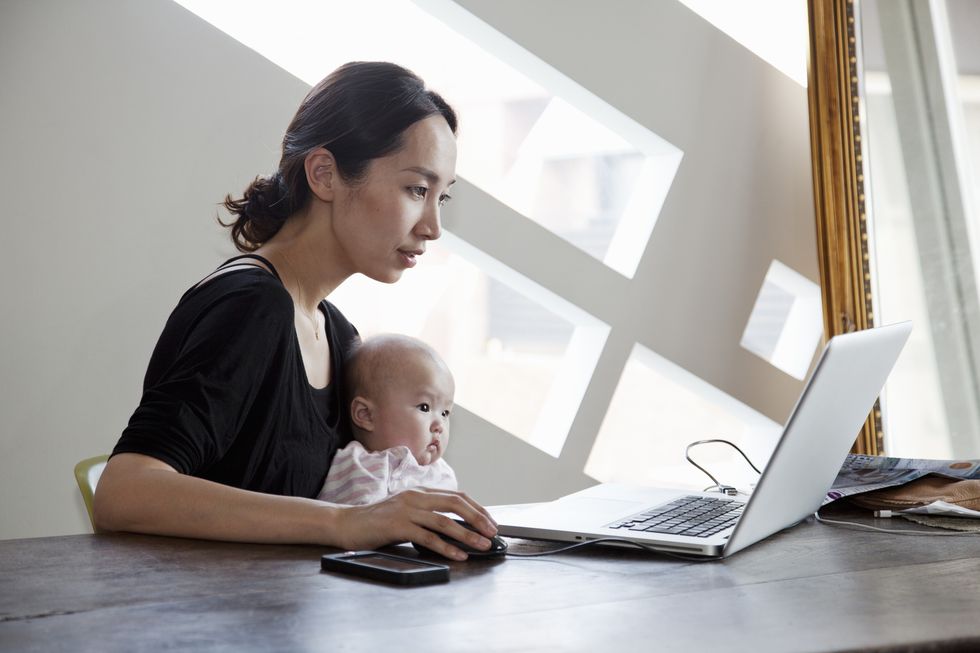 mother carrying her baby and working on laptop at home