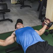 an asian man in a blue tank top does a set of dumbbell chest flys on a flat benchtraining pecs and upper body at the gym