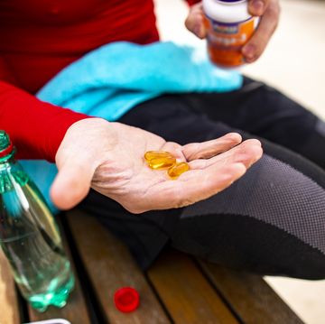 an athletic man holding out a couple of orange colored capsules on the palm of his hand while sitting on a park bench