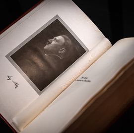 a book seen from overhead is open to a page with a portrait of a man looking left, an autograph signature is written below the picture