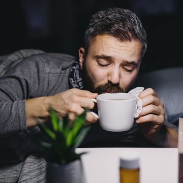 an ill mature man patient in bed at home, drinking hot tea