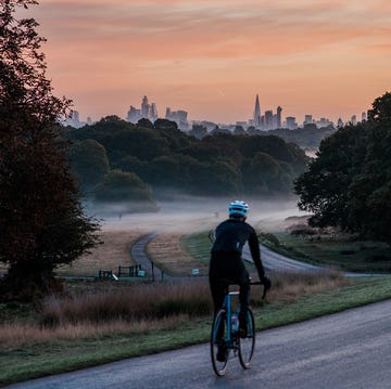 an unrecognisable cyclist on a winding road at dawn in a london park city of london in the background