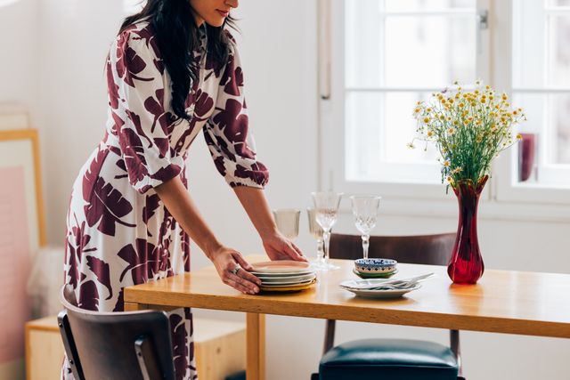an unrecognizable happy beautiful woman standing in the living room and preparing the table for lunch