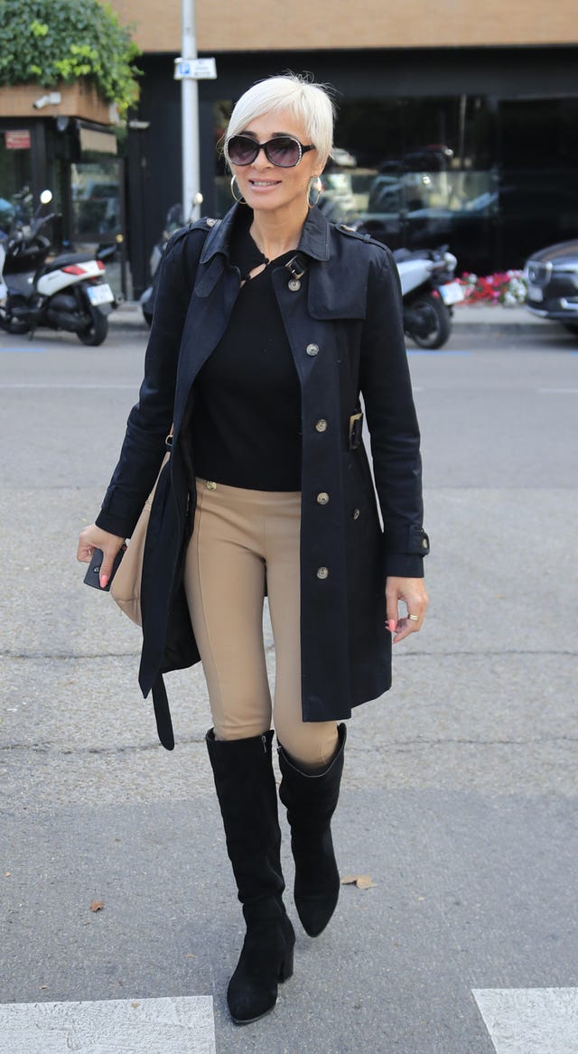 la ex de ortega cano con gafas de sol, gabardina negra, camiseta negra, pantalón beige y botas altas