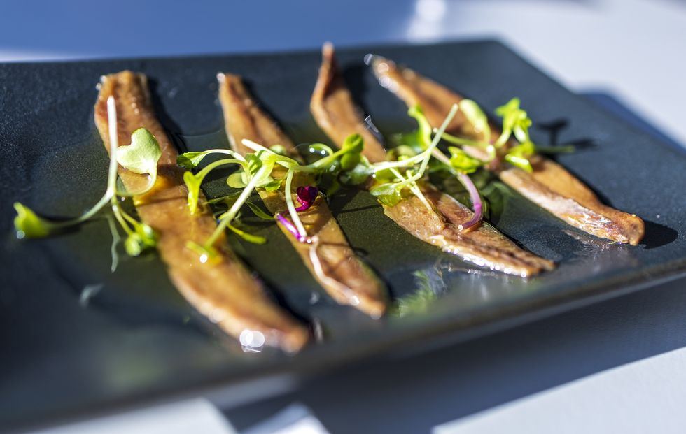 four anchovies arranged on a rectangular black plate, with some garnish.