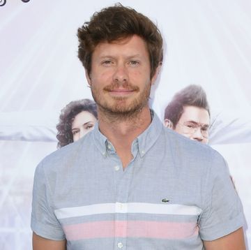 anders holm, a man stands with hands in his pockets, wearing cream trousers and blue shirt with cap sleeves