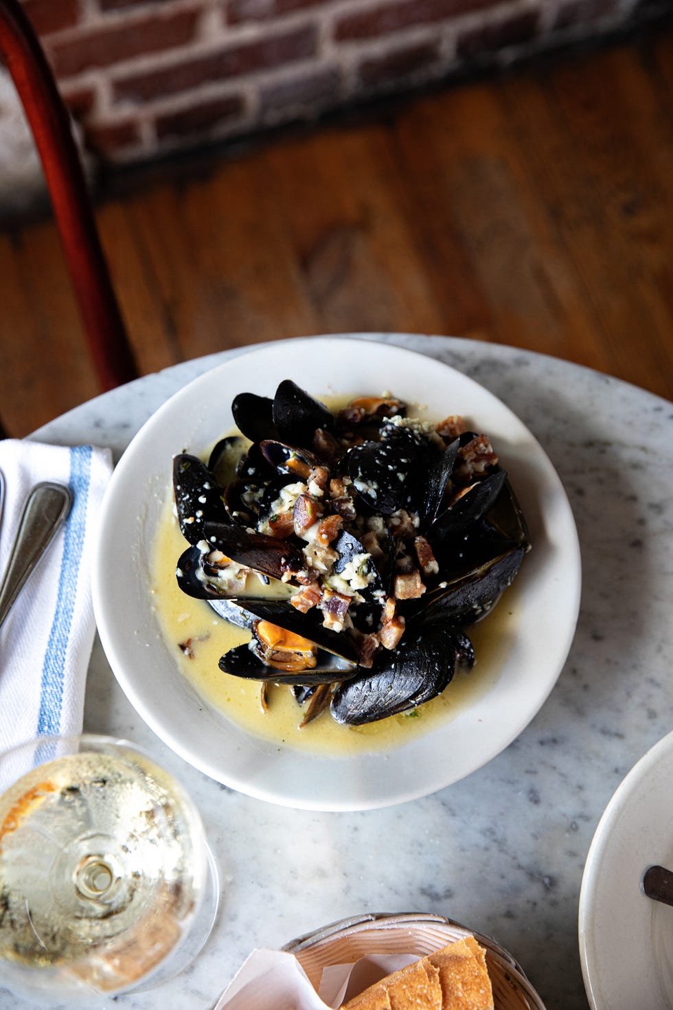A bowl of mussels in sauce with bacon bits on a table