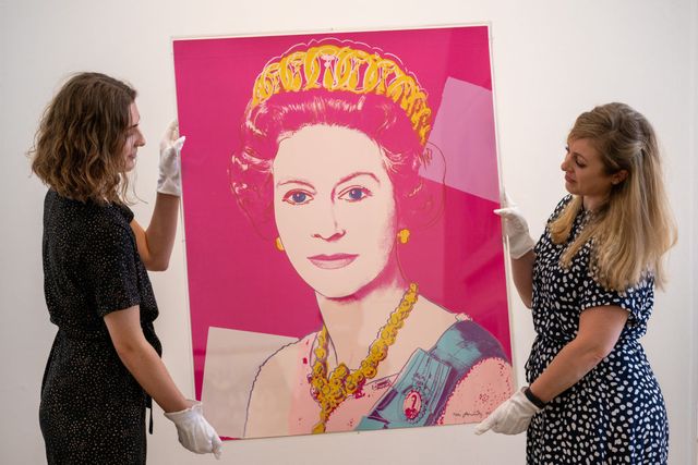 phillips auction house staff members hold a screen print of queen elizabeth ii by artist andy warhol in london