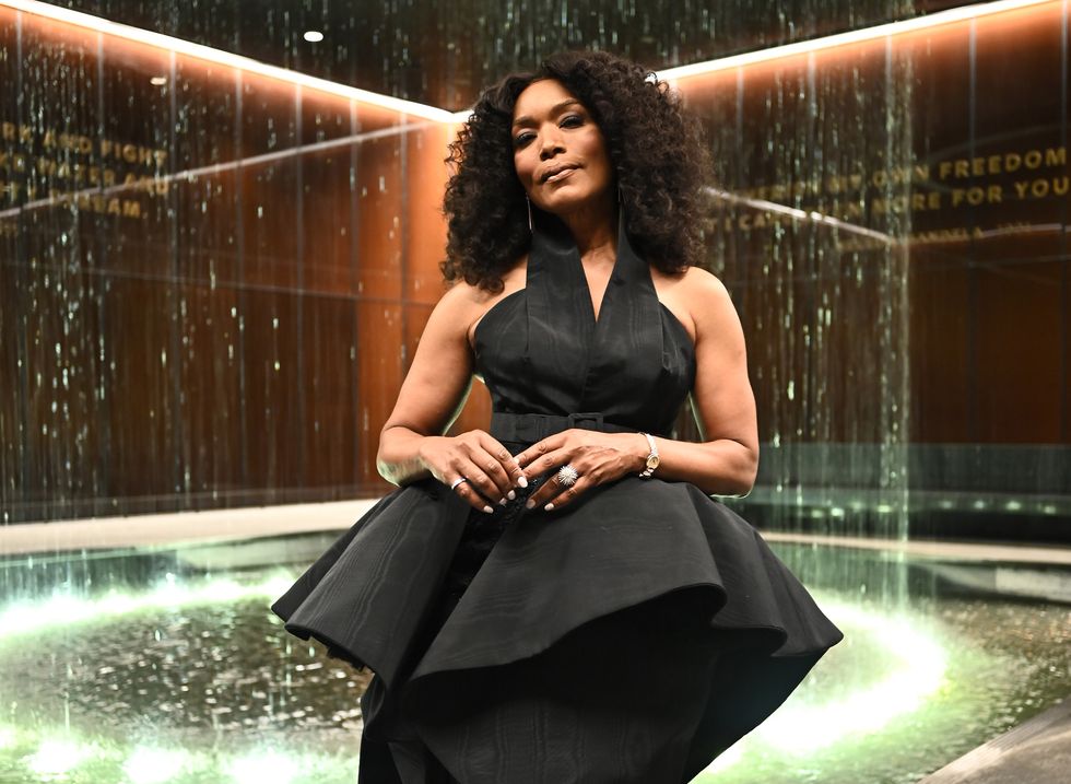 angela bassett wearing a black dress, holding her hands together, standing in front of a water fountain